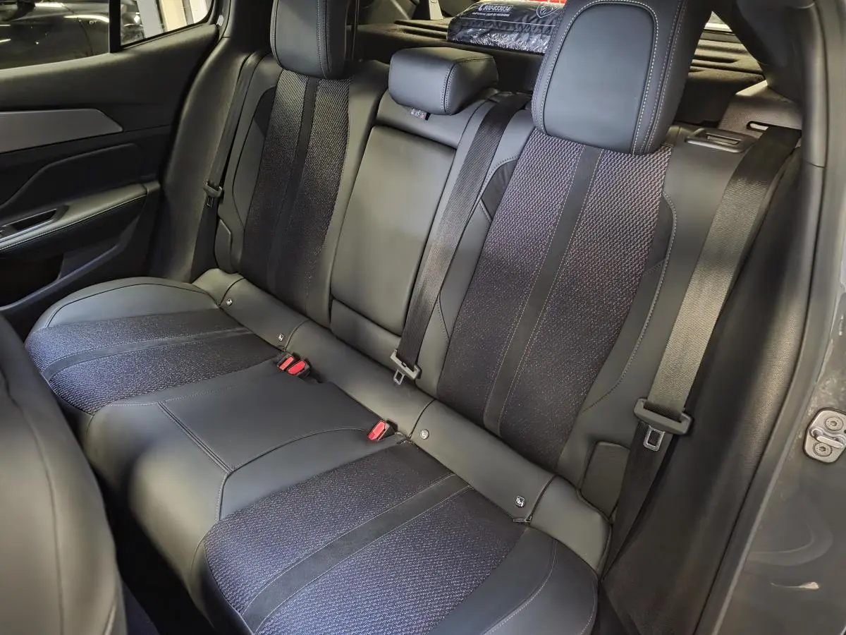 Vue intérieure de la banquette arrière en tissu et cuir noir du Peugeot 408 gris, avec ceinture de sécurité et appuis-tête.