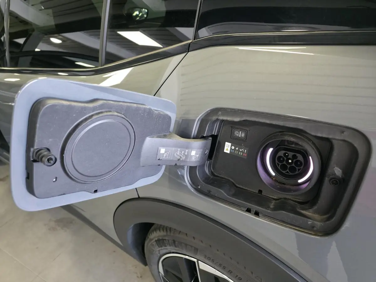 Prise de recharge ouverte côté arrière droit sur Peugeot 408 gris métallisé, avec jante alliage 19 pouces visible.