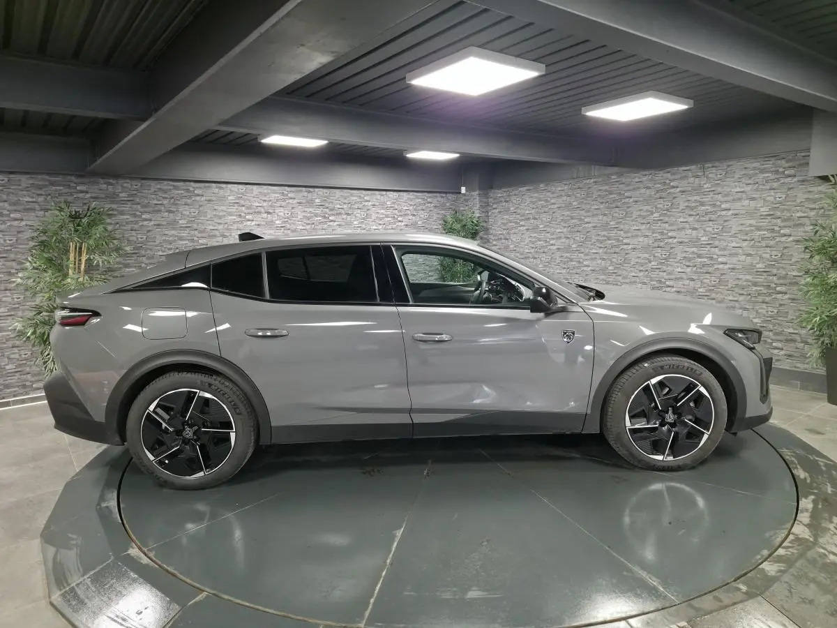 Vue latérale droite d'une Peugeot 408 gris métallisé avec jantes alliage noires et toit noir dans un showroom.