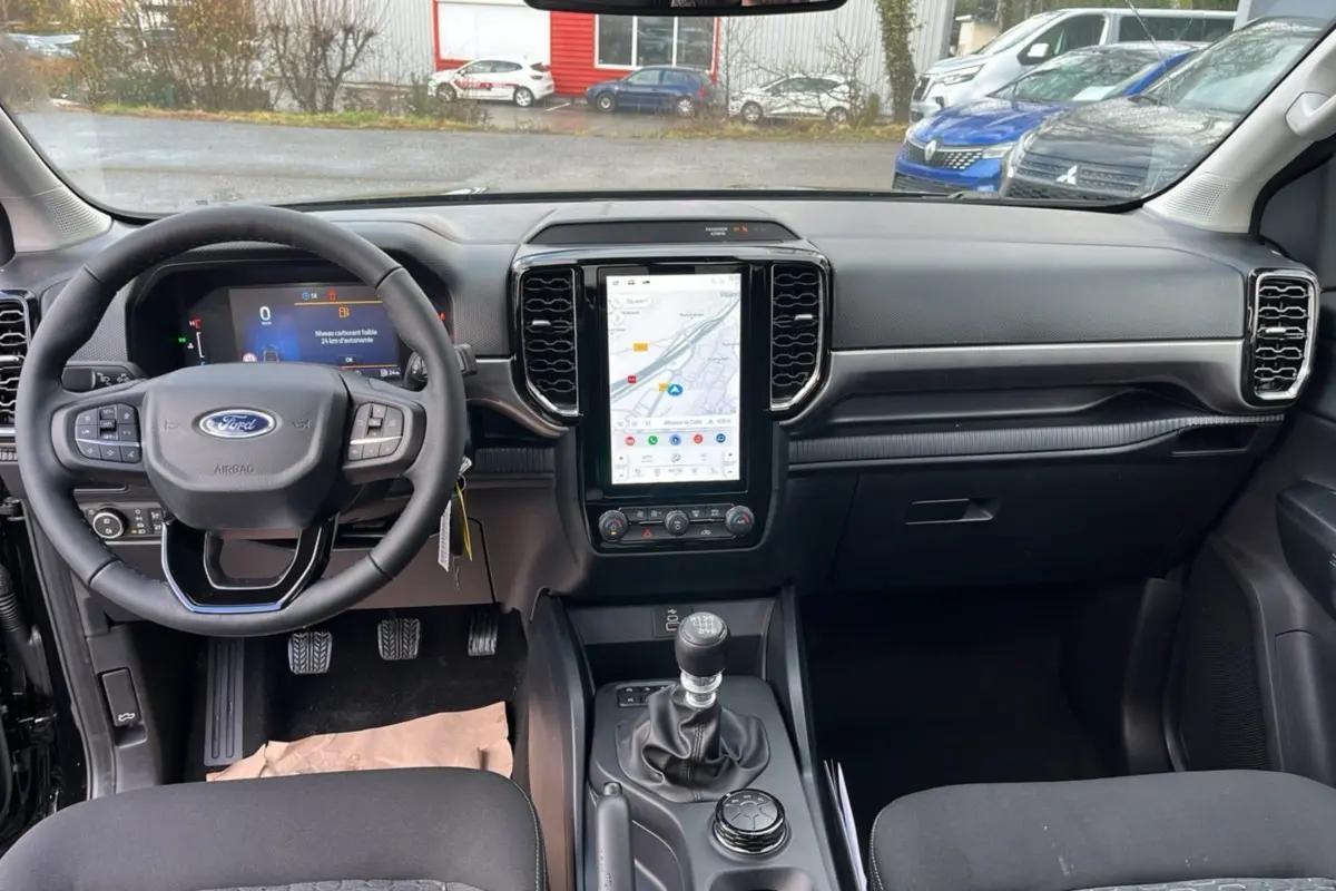 Vue intérieure avant du Ford Ranger noir shadow 2025, mettant en valeur le volant cuir multifonctions et l’écran tactile vertical.