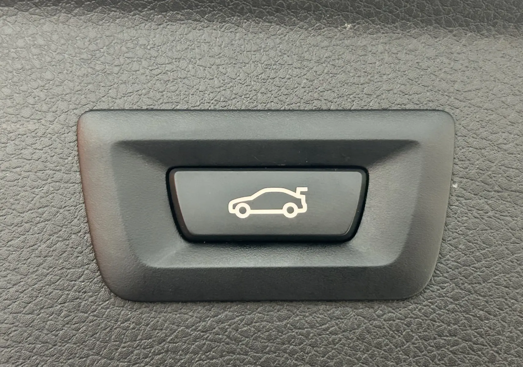 Bouton noir avec symbole blanc d'ouverture de coffre, sur panneau intérieur texturé noir d'une BMW Série 2 Active Tourer.