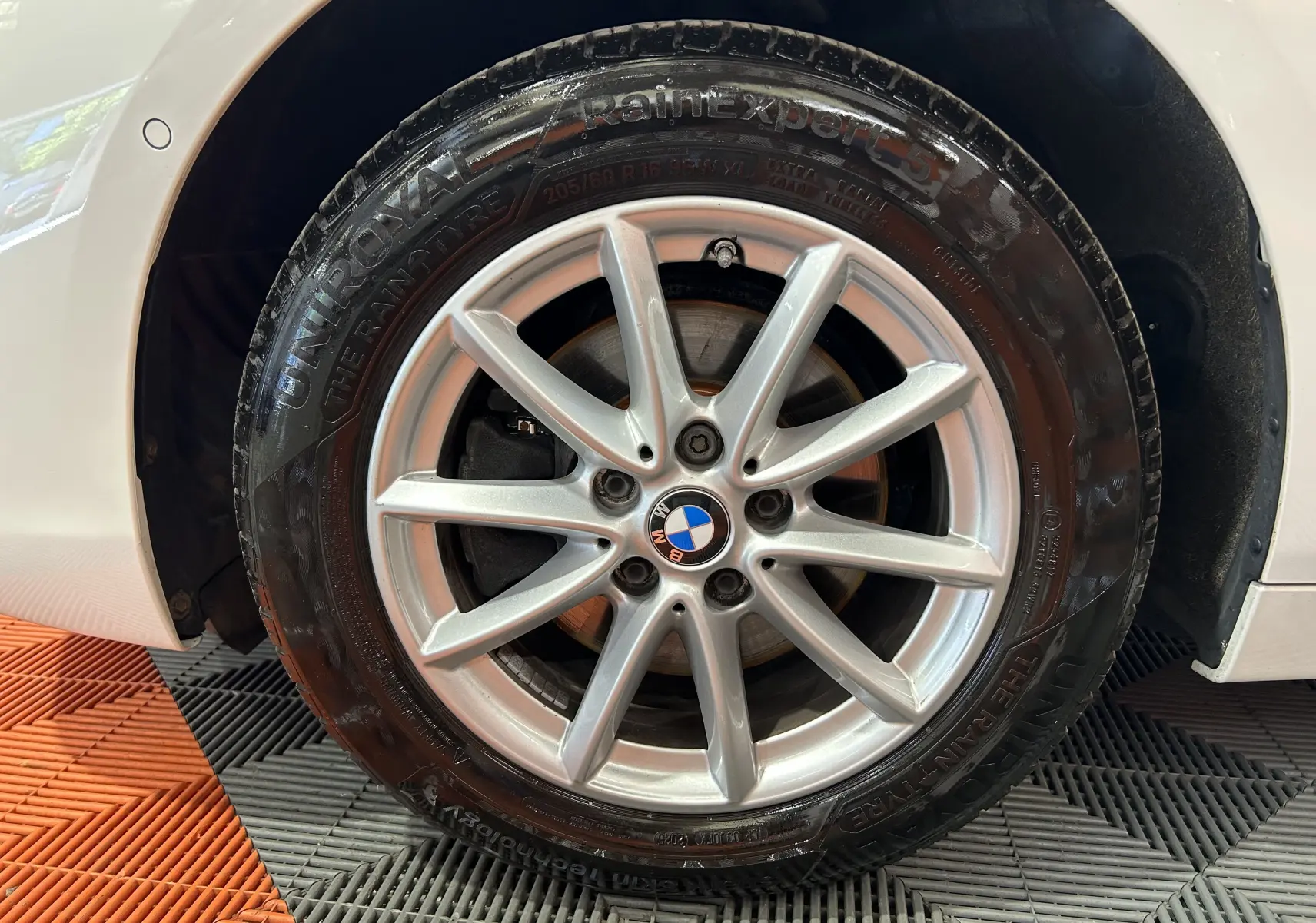 Gros plan sur la roue avant gauche blanche d'une BMW Série 2 Active Tourer 216d avec jante alliage argentée et logo BMW central.