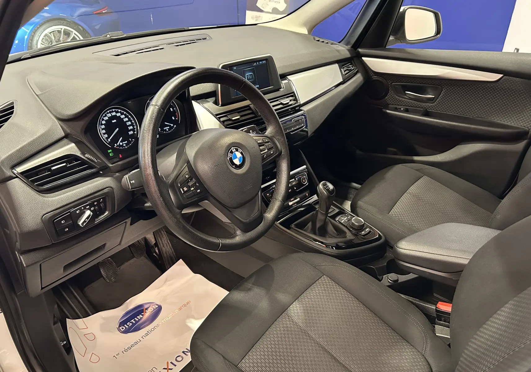 Vue intérieure côté conducteur de la BMW Série 2 Active Tourer 216d blanche, avec volant multifonction et boîte manuelle.