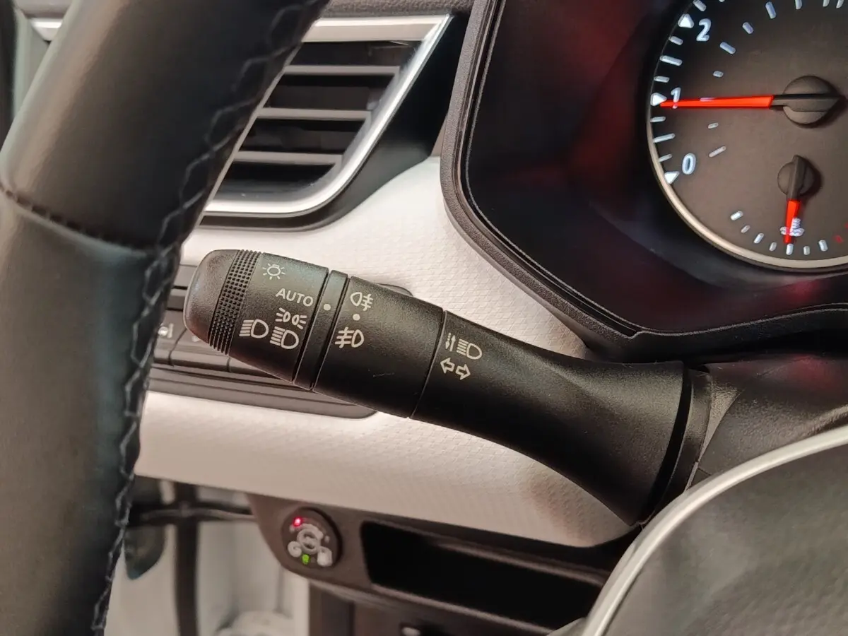 Gros plan sur la commande des phares à gauche du volant d’une Renault Clio blanche, tableau de bord clair visible.