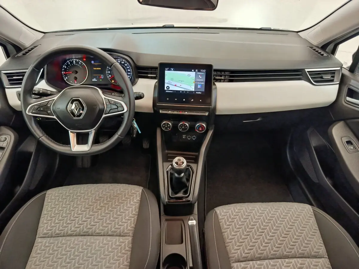 Vue intérieure avant de la Renault Clio blanche 2023, tableau de bord avec écran tactile central et volant multifonctions cuir.