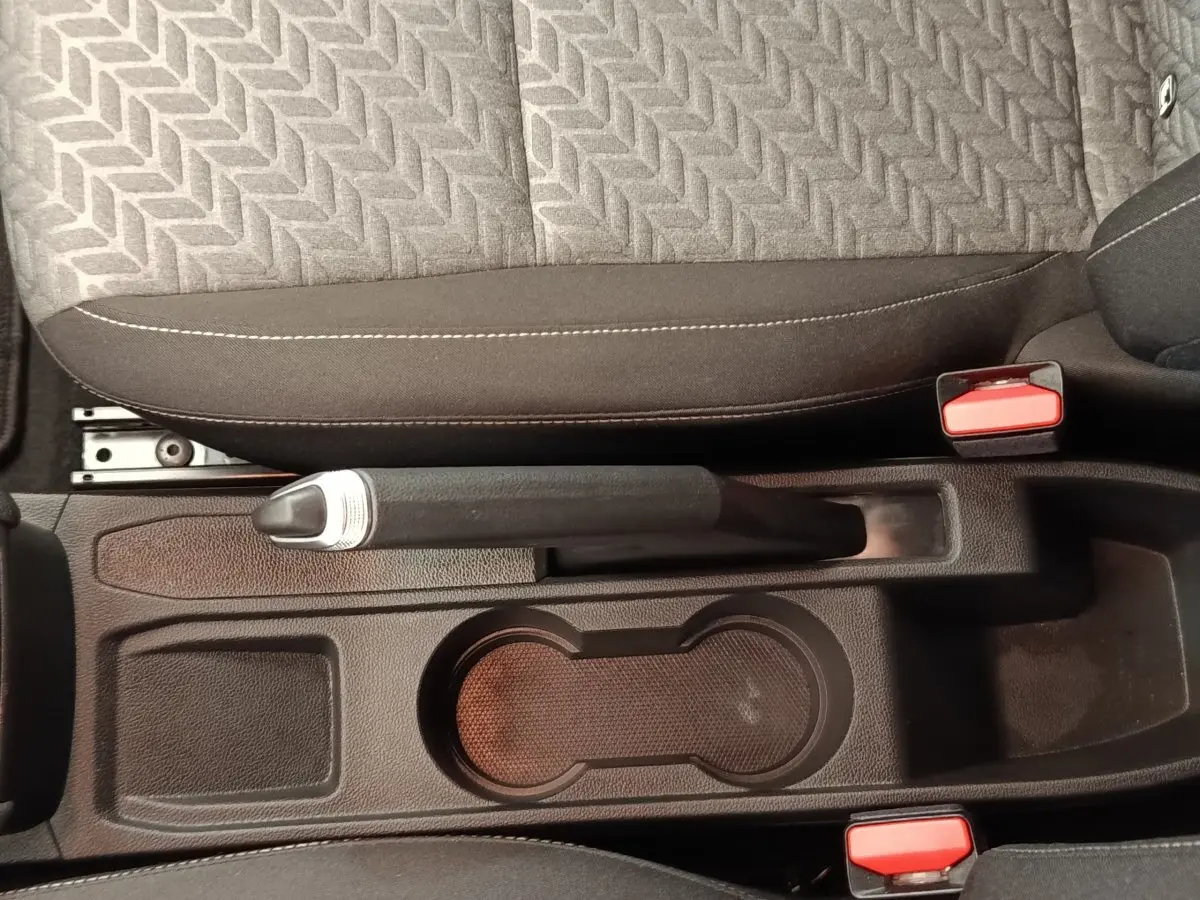Vue plongeante sur la console centrale noire de la Renault Clio avec frein à main manuel et porte-gobelets.