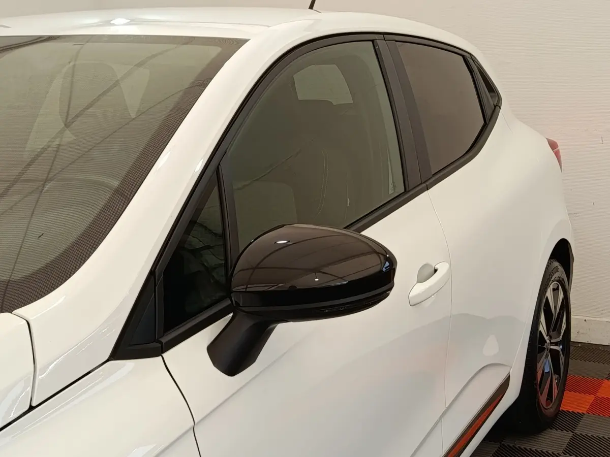 Vue côté gauche avant d'une Renault Clio blanche avec rétroviseur noir brillant et vitres teintées.