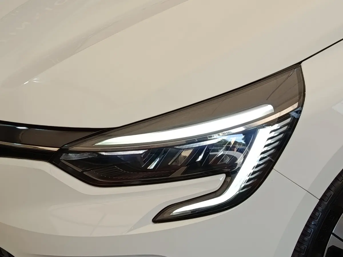 Gros plan sur le phare avant droit allumé d'une Renault Clio Evolution TCe 100 GPL blanche de 2023.