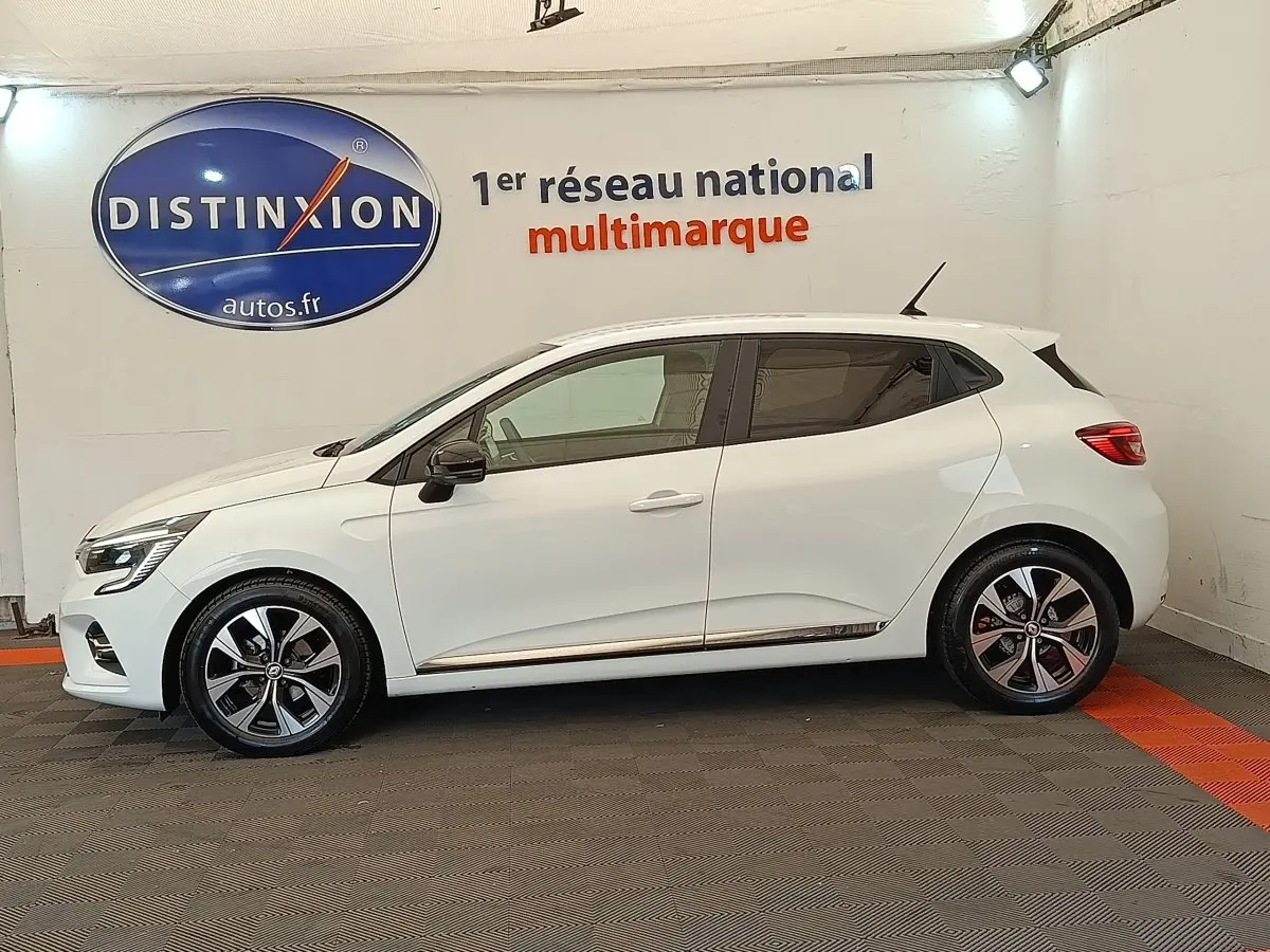 Profil droit d'une Renault Clio Evolution TCe 100 GPL blanche avec jantes alliage et rétroviseurs noirs en intérieur showroom.