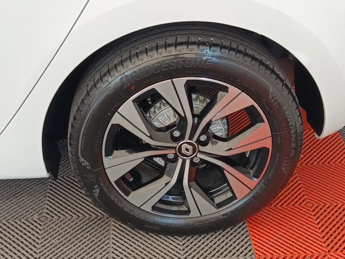 Gros plan sur la roue avant gauche d'une Renault Clio blanche, mettant en valeur la jante alliage au design moderne.