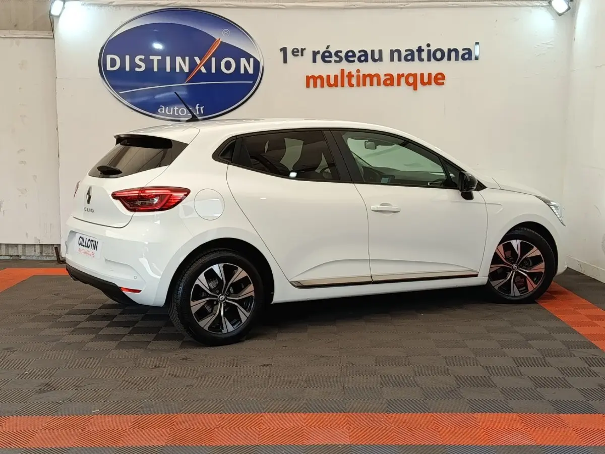 Profil droit d'une Renault Clio blanche Evolution TCe 100 GPL 2023, avec jantes alliage et vitres teintées, en intérieur showroom.