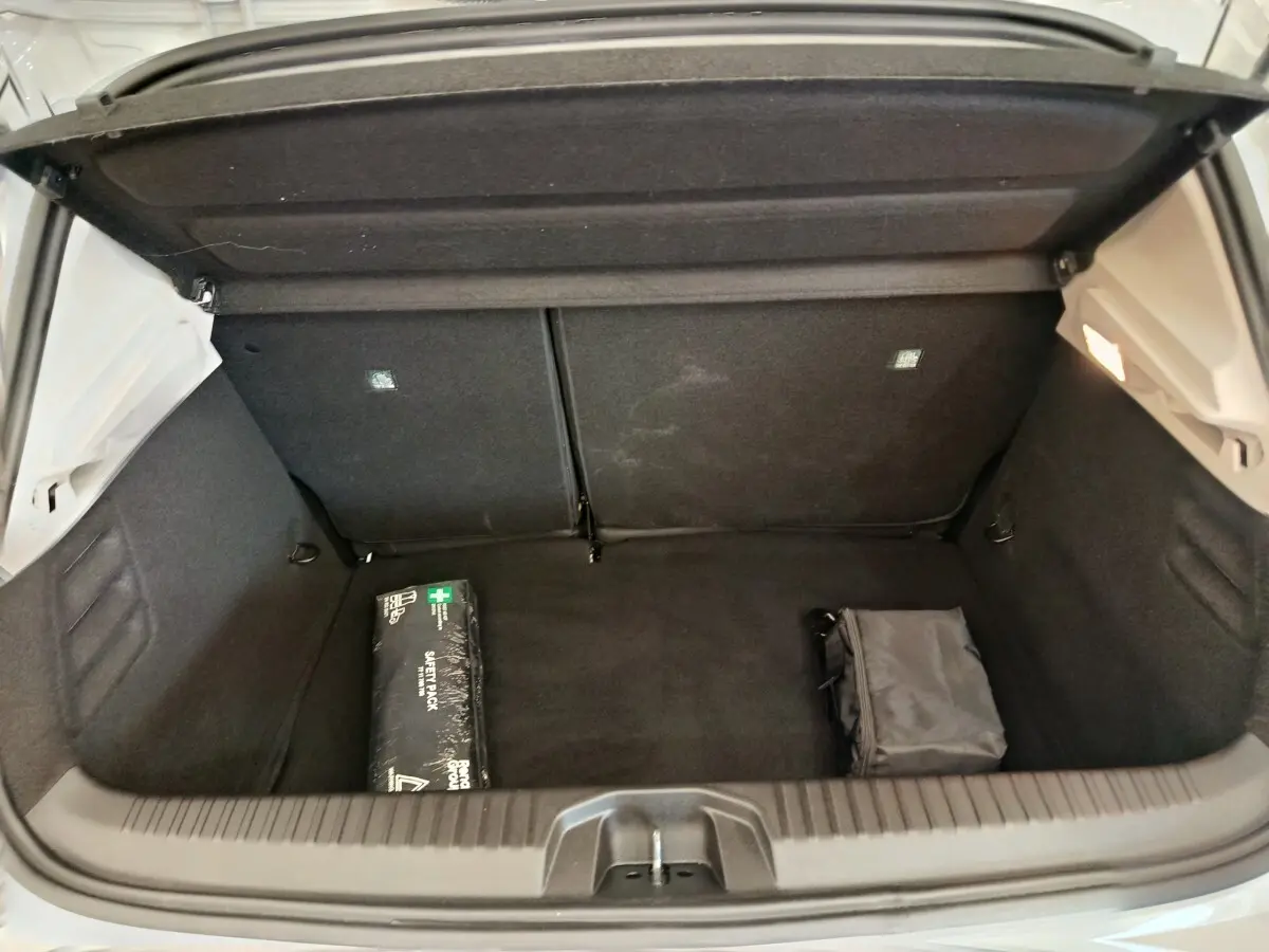 Coffre ouvert de Renault Clio blanc, vue de l'arrière montrant un espace de rangement avec trousse de secours et sac noir.