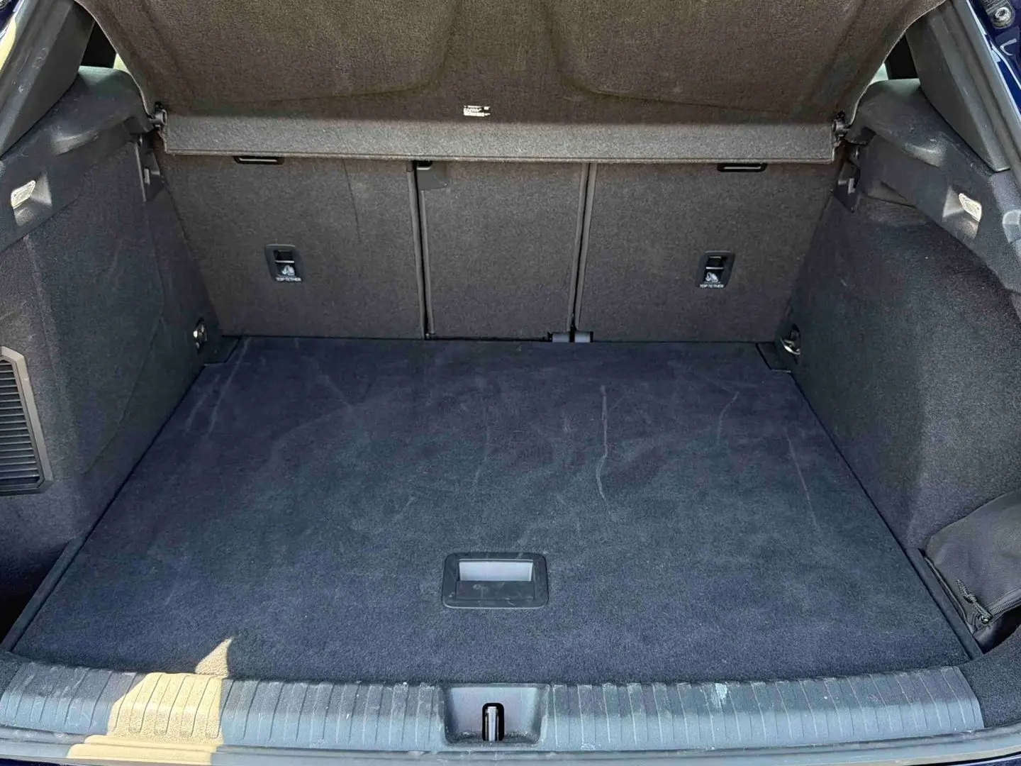 Coffre ouvert vu de l'arrière d'une CUPRA Terramar bleu, espace de chargement avec tapis noir et habillage intérieur sombre.