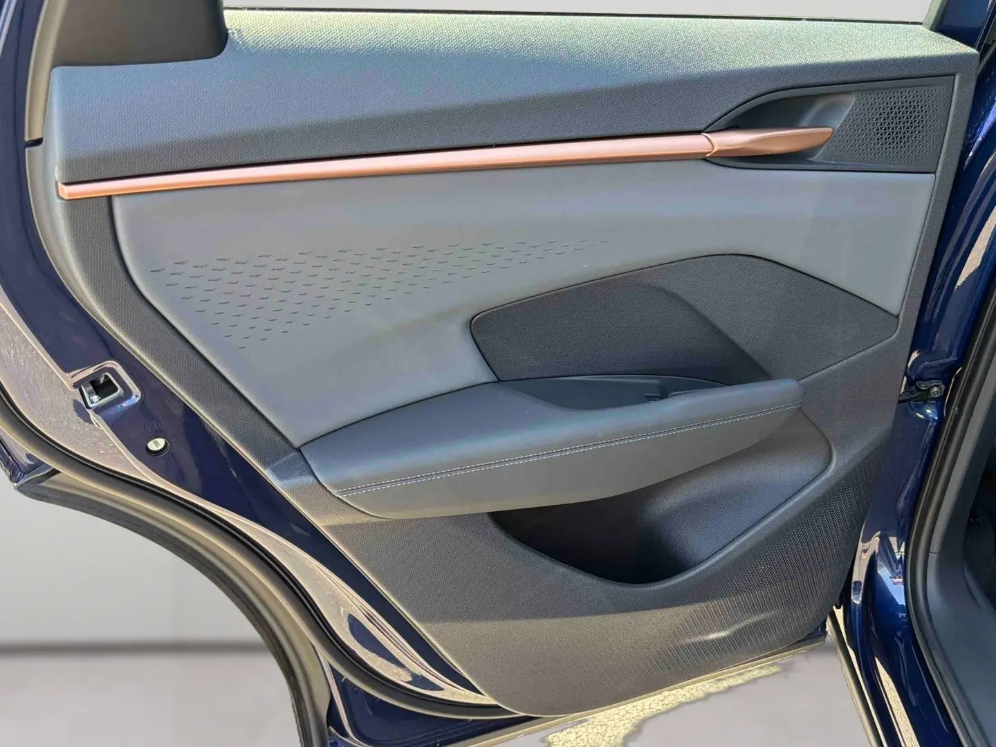 Vue rapprochée de la porte arrière gauche bleu cosmos du CUPRA Terramar avec insert cuivré et garniture noire texturée.