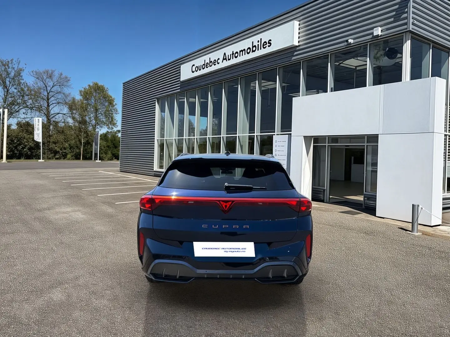 Vue arrière d'une CUPRA Terramar 2025 bleu cosmos avec bandeau lumineux et logo CUPRA rouge, stationnée devant un concessionnaire.