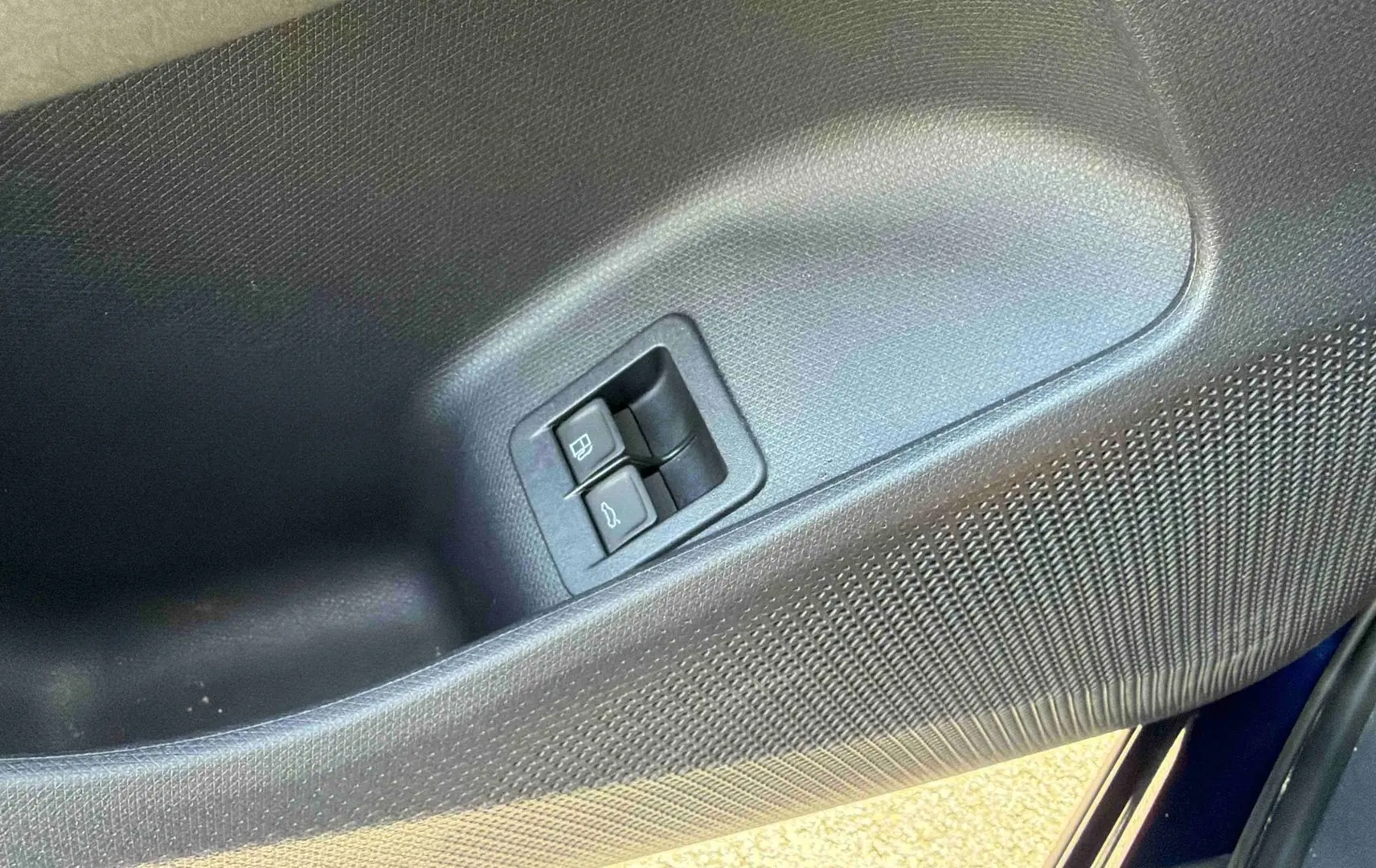 Gros plan sur la porte côté gauche de la CUPRA Terramar bleue, montrant les boutons d'ouverture du coffre et de la trappe à carburant.