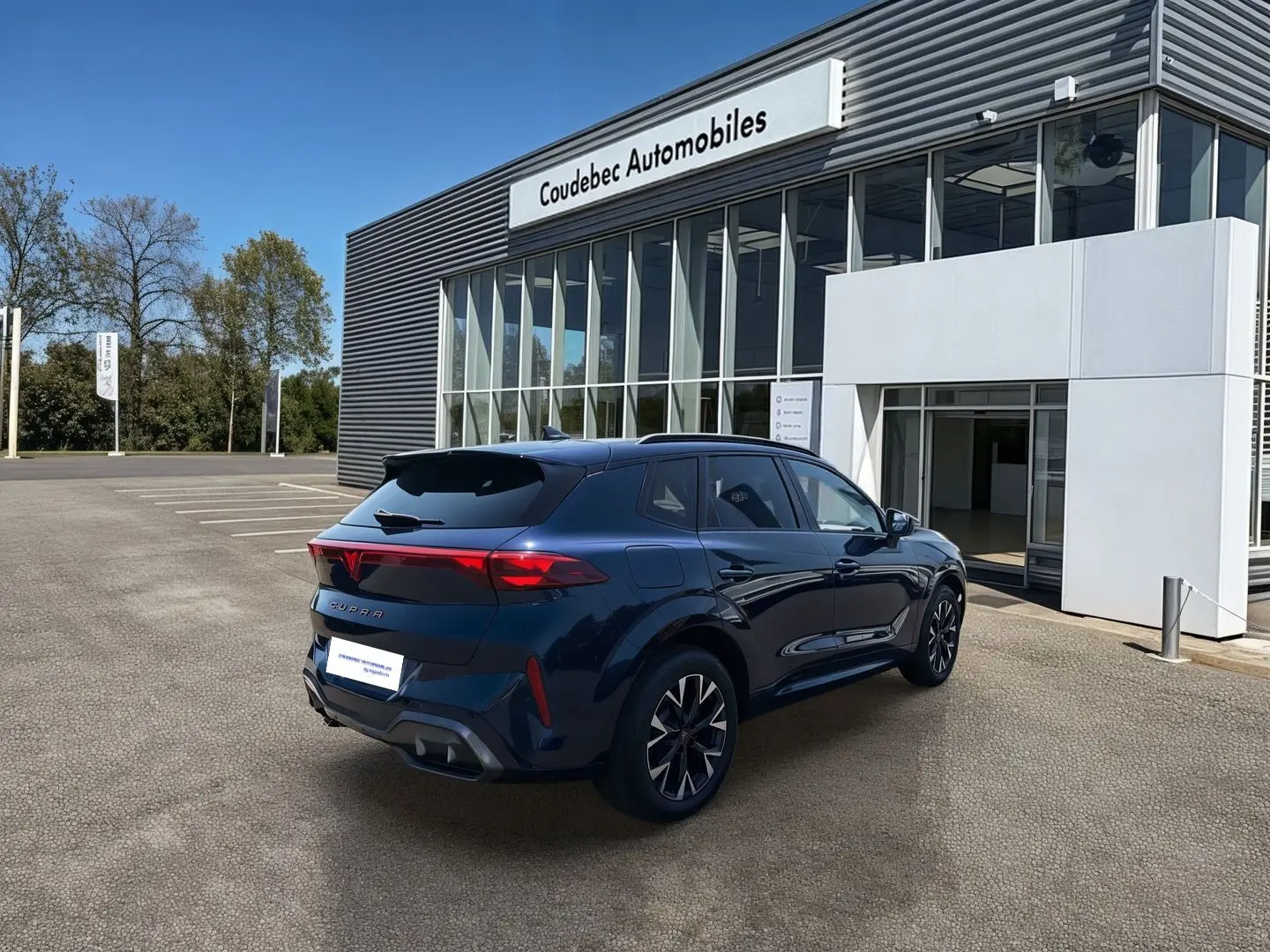 Vue 3/4 arrière droite d’un CUPRA Terramar bleu métallisé devant un bâtiment de concession Coudebec Automobiles.