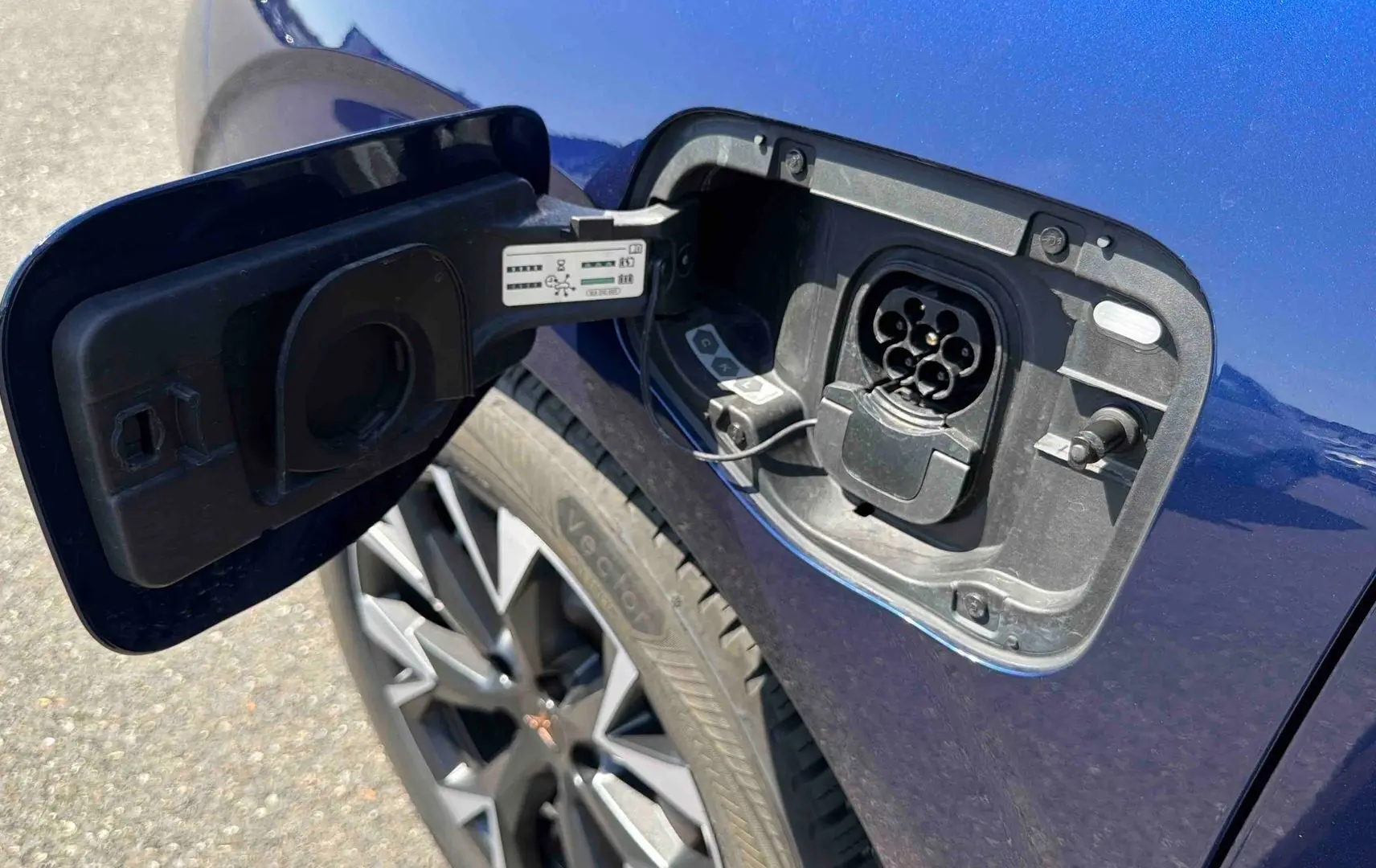 Prise de recharge électrique ouverte côté gauche sur une CUPRA Terramar bleue avec jante alliage visible.
