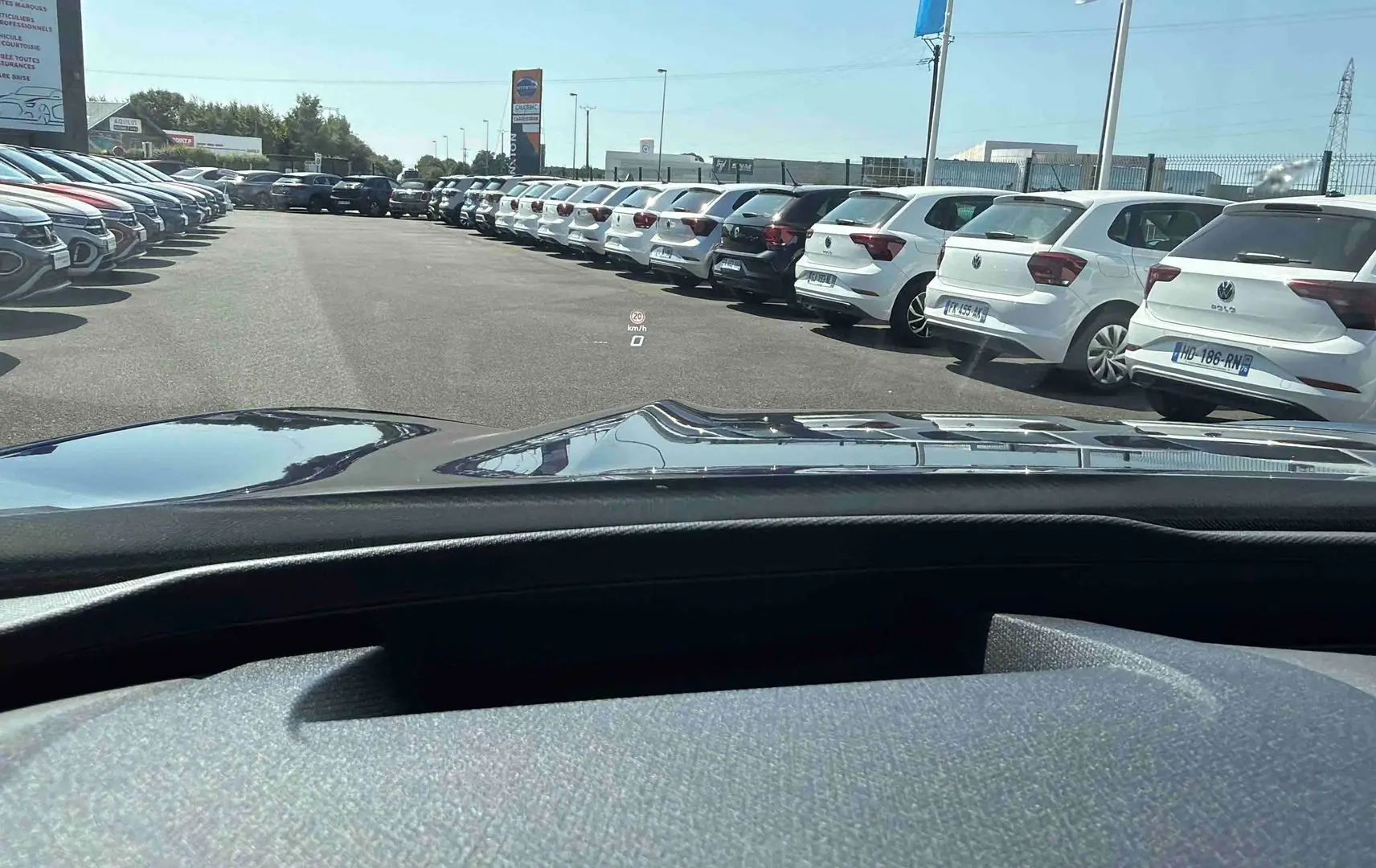 Vue depuis l’habitacle d’un CUPRA Terramar bleu, montrant le capot et un parking de voitures blanches à l’extérieur.