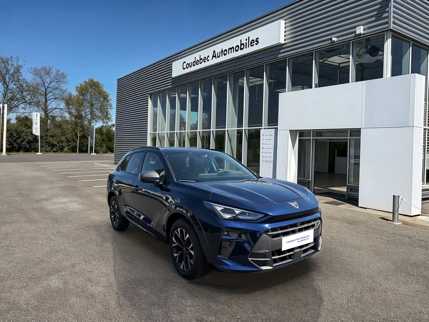 Vue 3/4 avant d'un CUPRA Terramar bleu métallisé garé devant un bâtiment moderne de concession automobile.