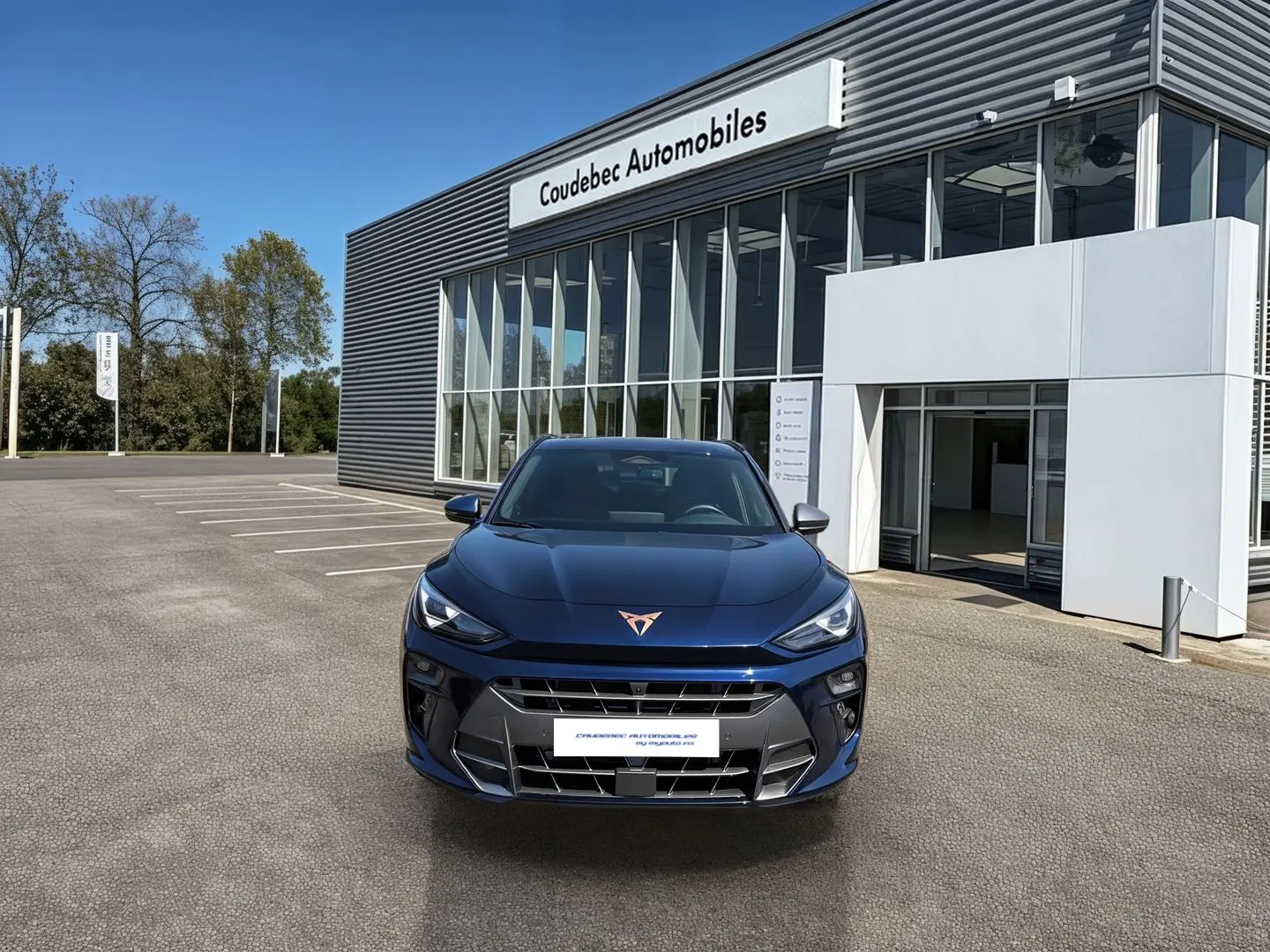 Vue avant d'une CUPRA Terramar 2025 bleu métallisé avec logo cuivré, stationnée devant un concessionnaire.