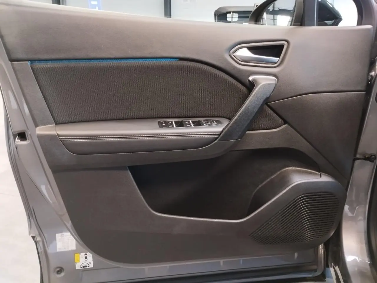 Porte intérieure côté gauche gris cassiopée de Renault Symbioz 2025 avec commandes de vitres et haut-parleur intégré.