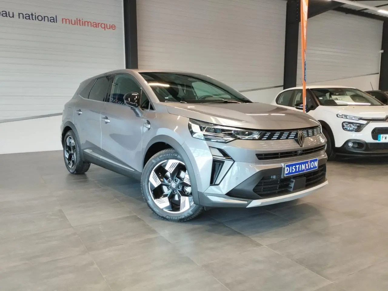 Renault Symbioz gris Cassiopée en 3/4 avant droit, avec jantes alliage noires et chromées, en intérieur showroom.