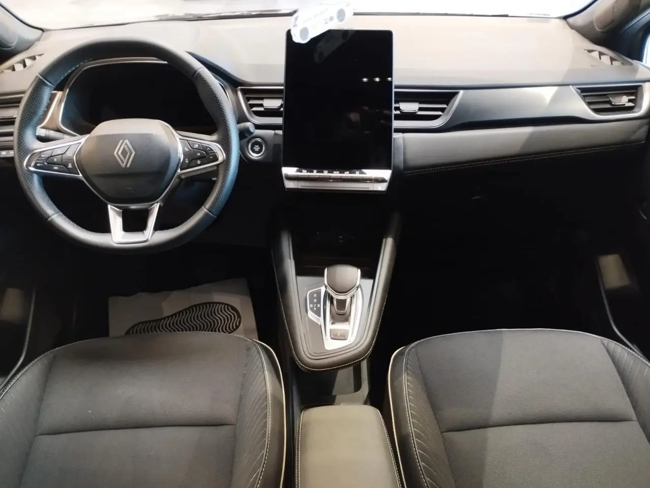Vue intérieure avant du tableau de bord et console centrale noire du Renault Symbioz avec écran tactile vertical.