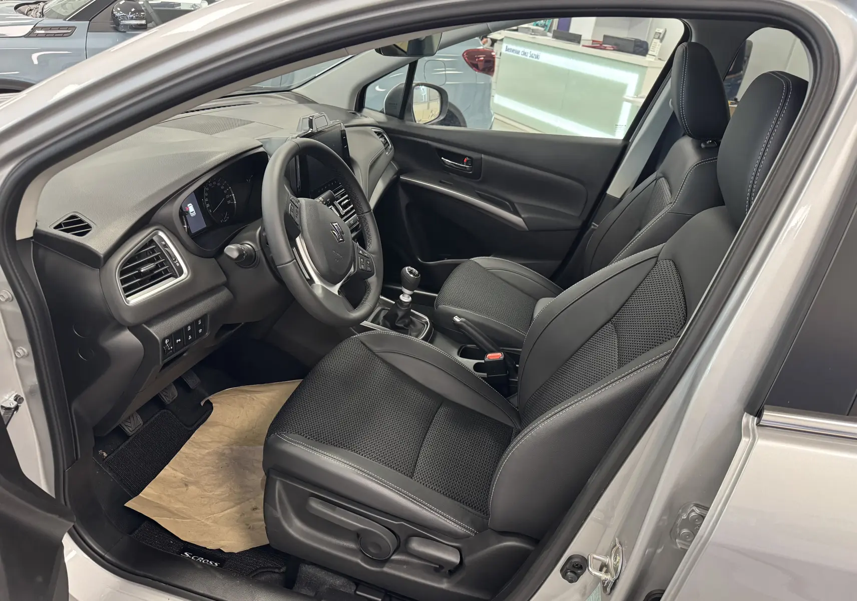 Intérieur du Suzuki S-Cross 2025 gris, vue côté conducteur, sièges noirs en cuir et tableau de bord moderne.