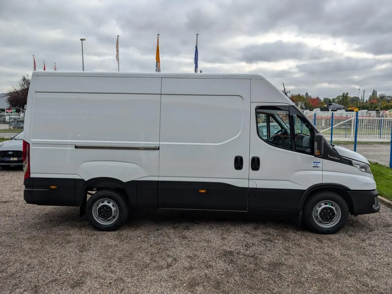 Fourgon Iveco Daily blanc vu de profil côté gauche avec portes coulissantes et protections noires basses.