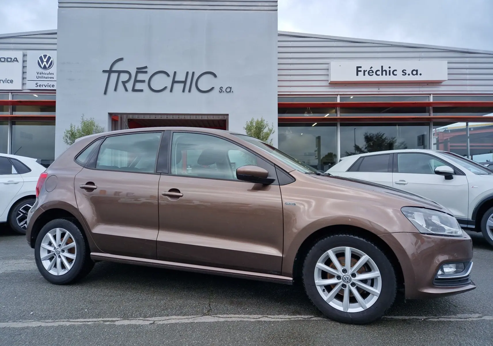 Vue de profil côté gauche d'une Volkswagen Polo 1.4 TDI 2015 brun métallisé stationnée devant un garage.