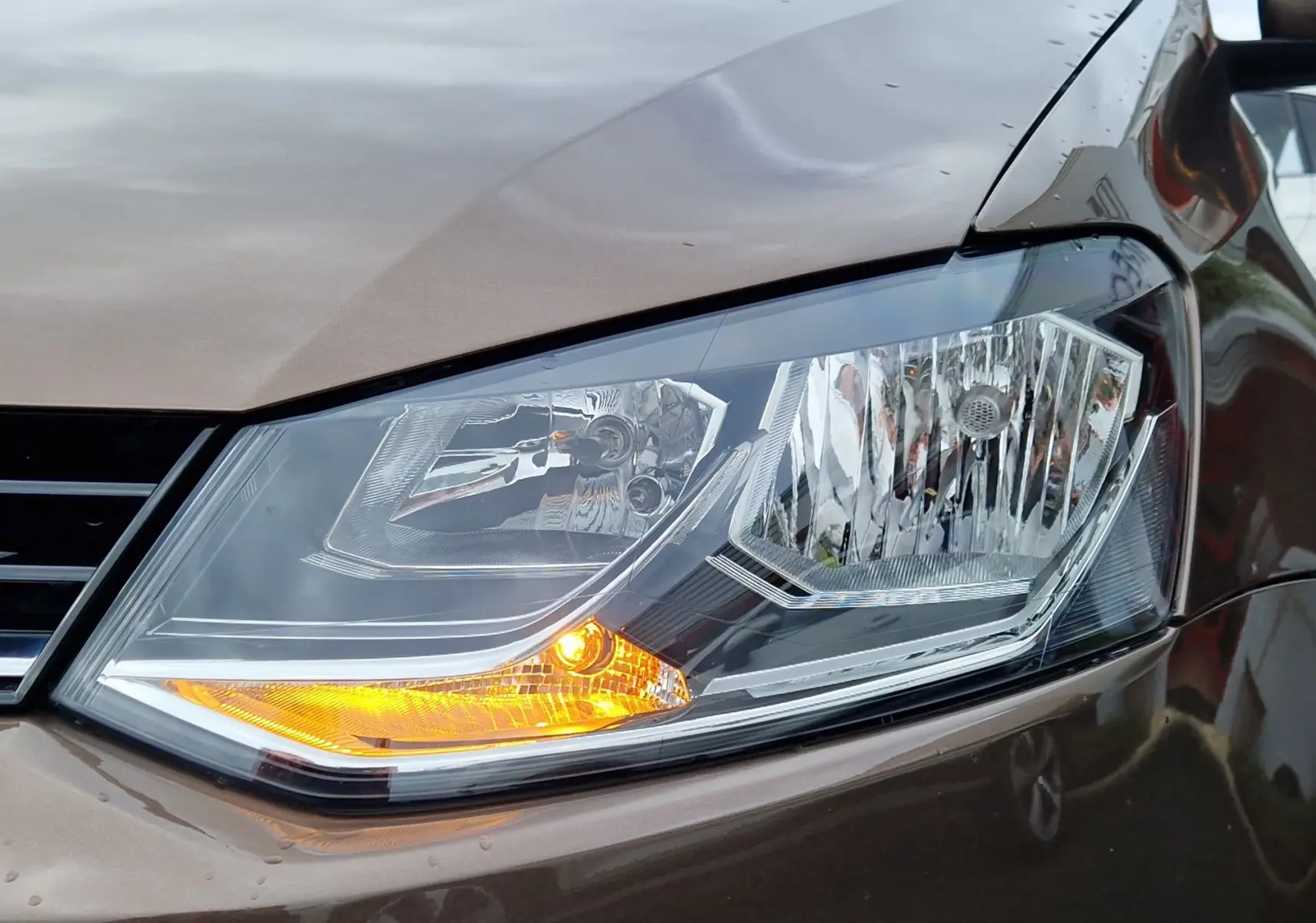 Gros plan sur le phare avant droit allumé d'une Volkswagen Polo 2015 brun métallisé, finition Lounge.