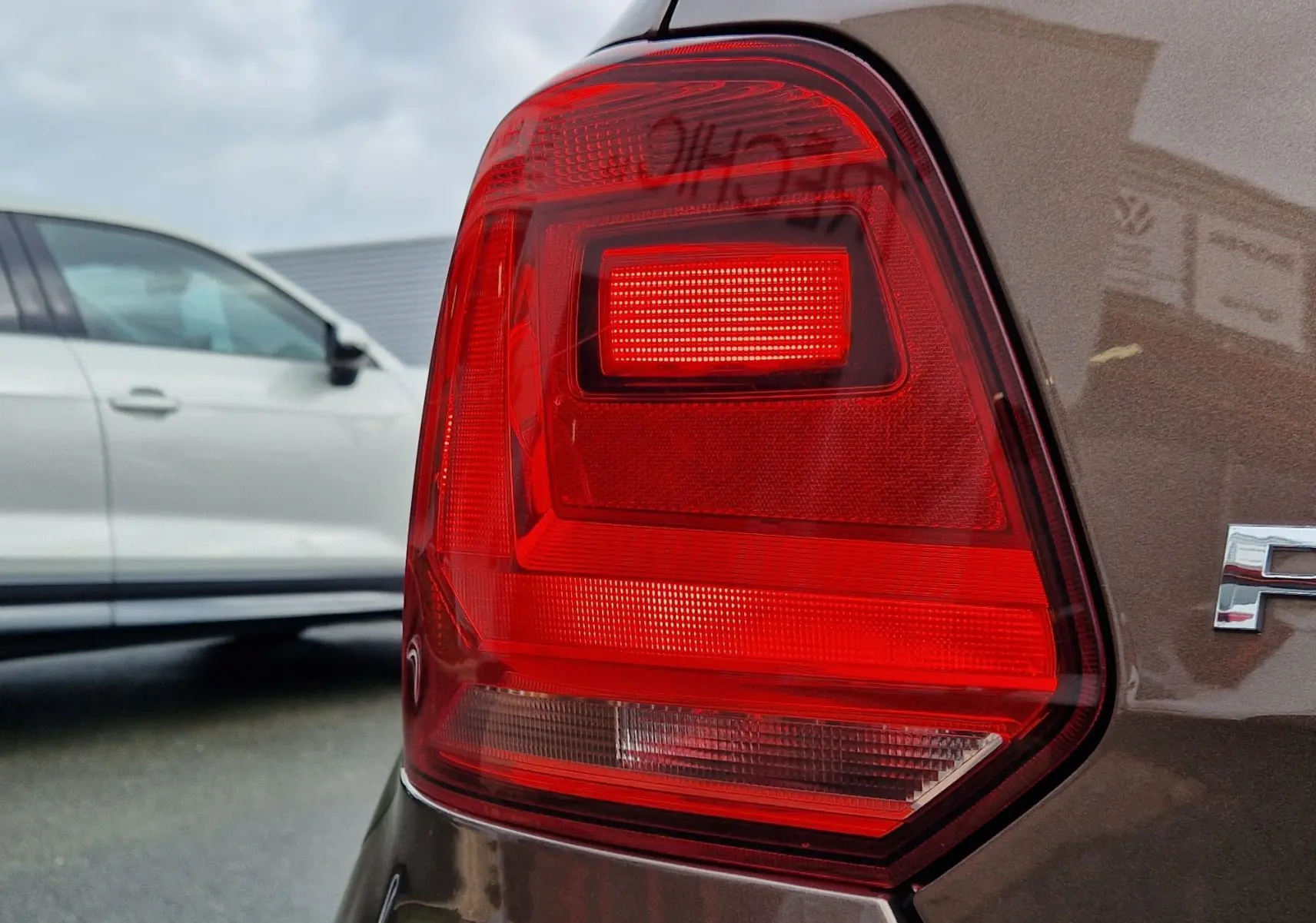 Gros plan sur le feu arrière droit d’une Volkswagen Polo 1.4 TDI brun 2015, finition Lounge, avec reflet du logo VW.
