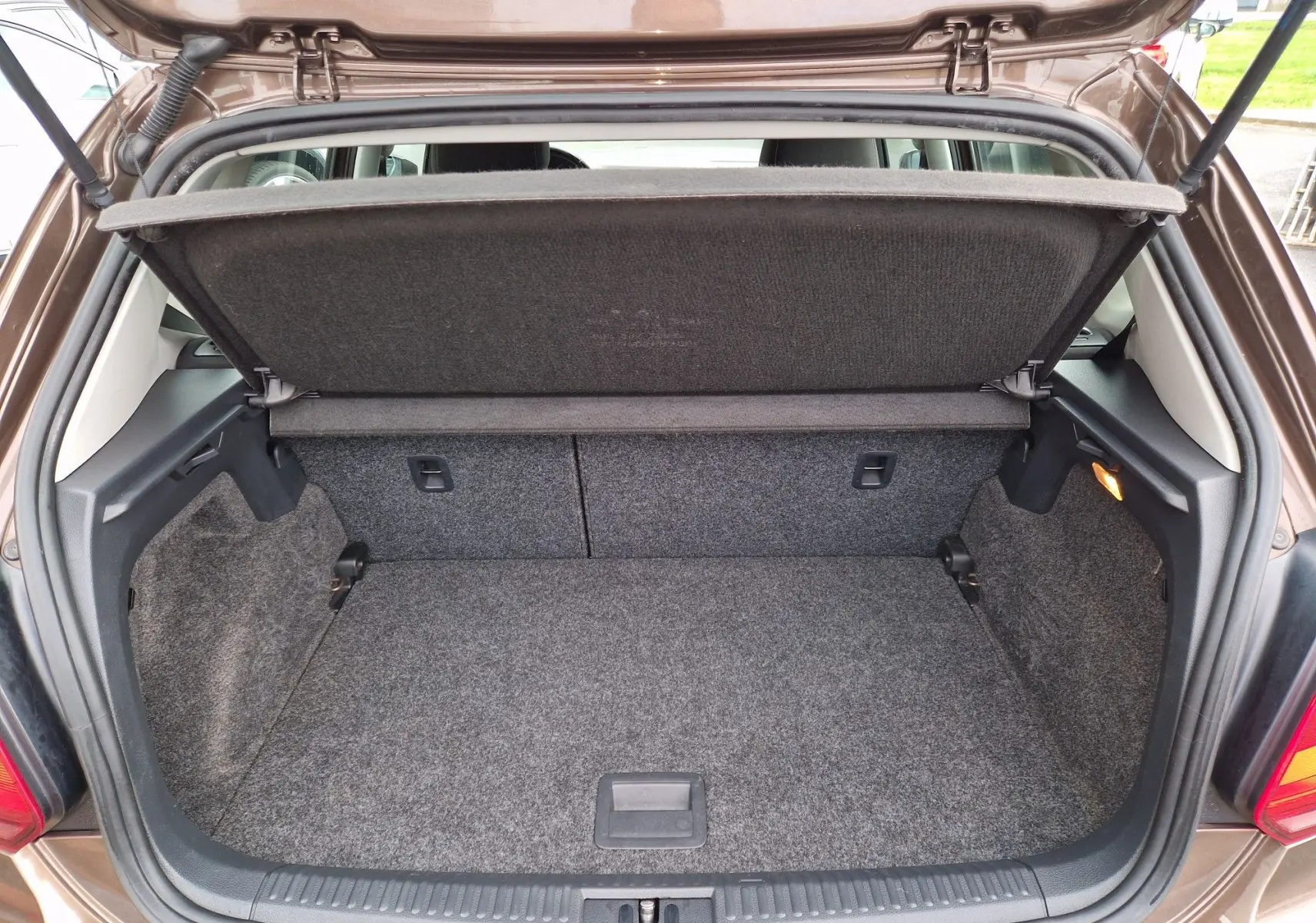 Coffre ouvert vu de l'arrière d'une Volkswagen Polo 1.4 TDI 2015 brun avec tapis de coffre gris et cache-bagages relevé.