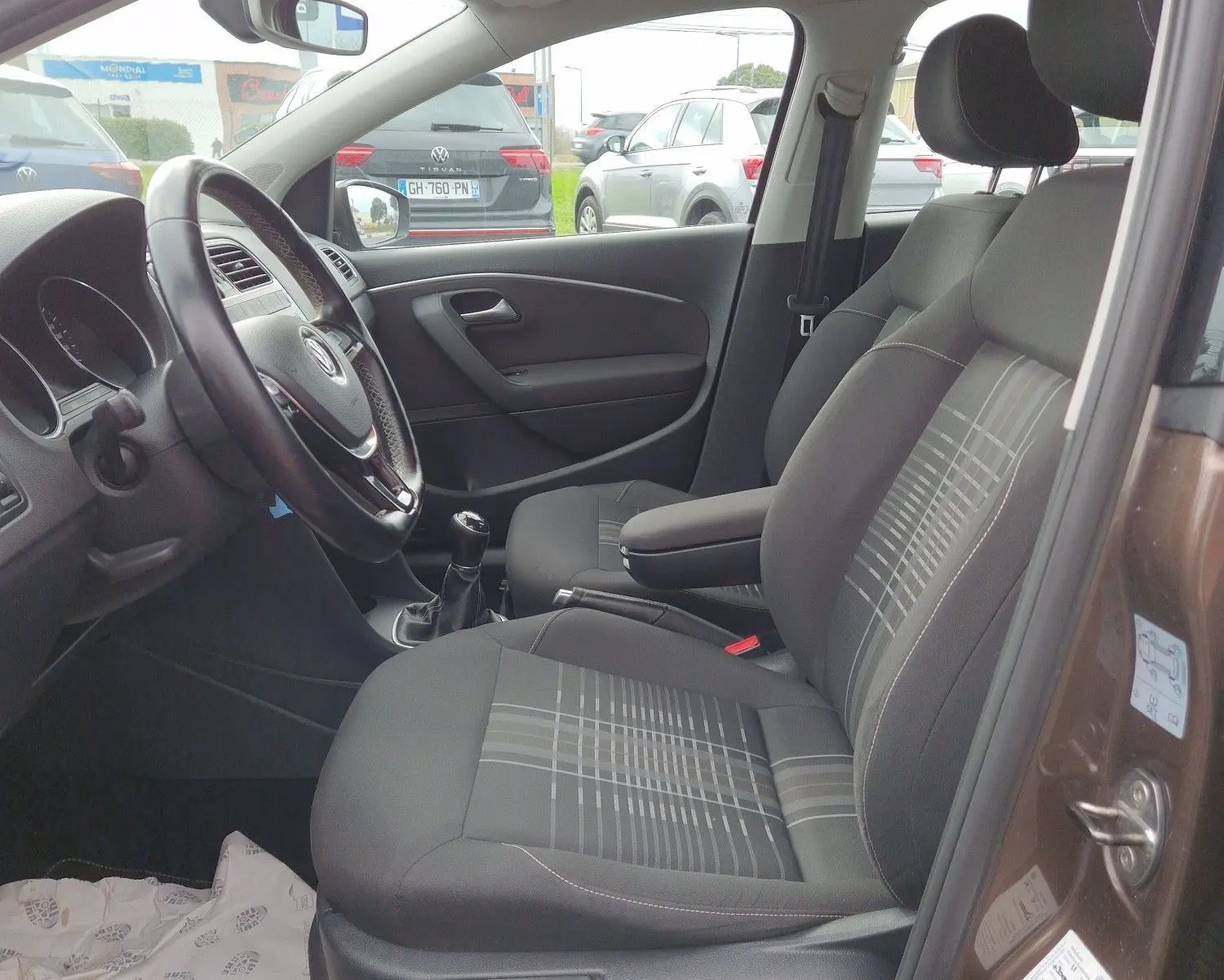 Vue intérieure côté conducteur de la Volkswagen Polo 1.4 TDI brun 2015, sièges tissu à motifs et volant cuir multifonction.