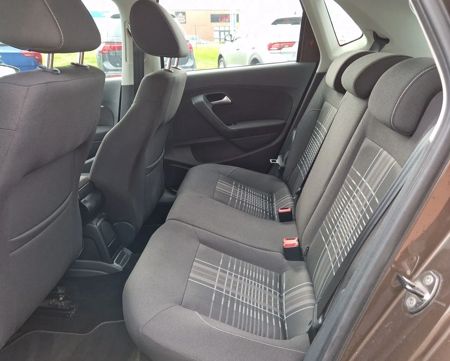 Vue intérieure côté droit des sièges arrière en tissu gris à motifs de la Volkswagen Polo 1.4 TDI brun 2015, porte ouverte.