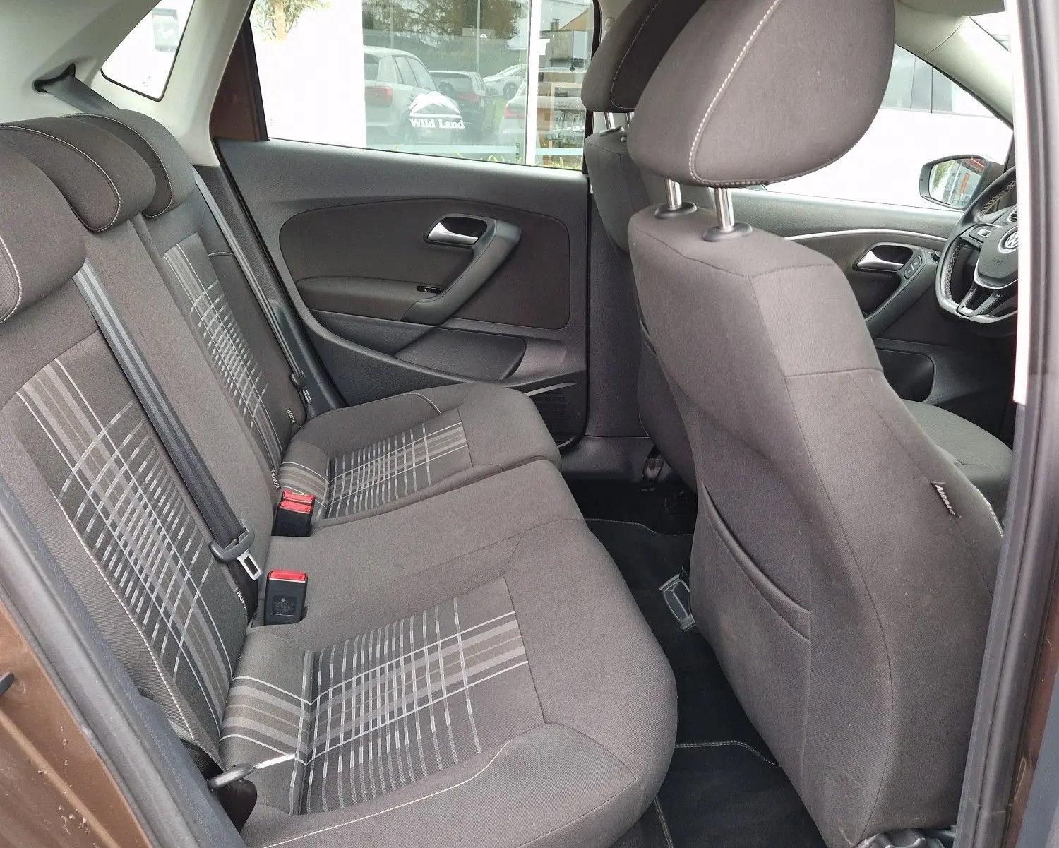 Vue intérieure côté gauche arrière de la Volkswagen Polo 1.4 TDI 2015 brun, montrant les sièges tissu à motifs et l'habitacle spacieux.