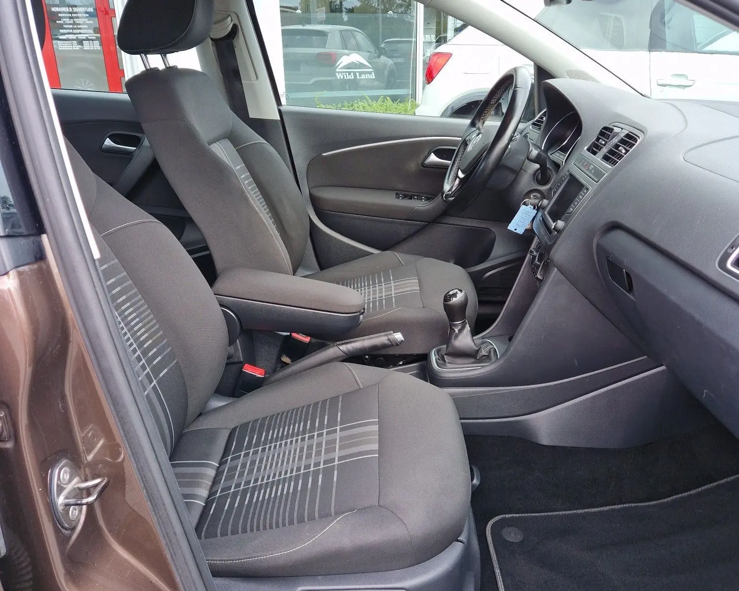 Vue intérieure côté conducteur d'une Volkswagen Polo 2015 brun 4Q4Q, finition Lounge avec sièges tissu à motifs et boîte manuelle.