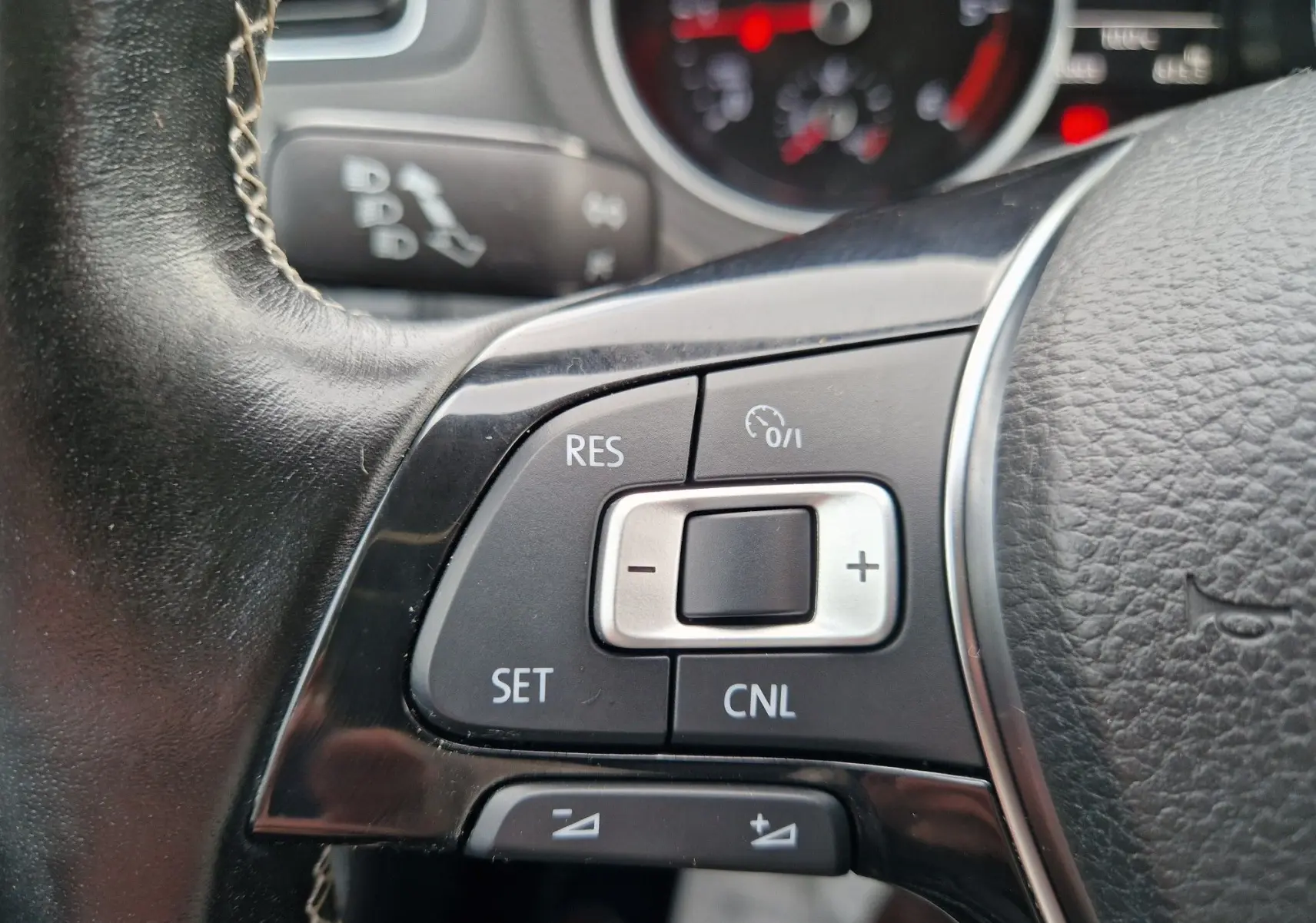 Gros plan sur les commandes de régulateur de vitesse au volant cuir noir de la Volkswagen Polo 2015 finition Lounge.