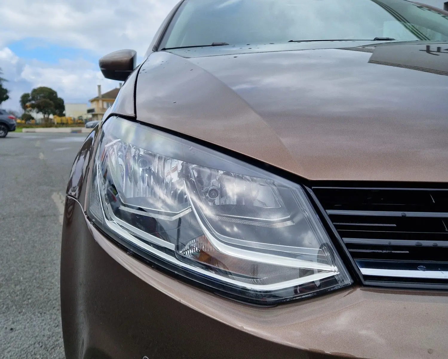 Gros plan sur l'avant gauche d'une Volkswagen Polo 2015 brun métallisé, mettant en valeur son phare et la calandre.