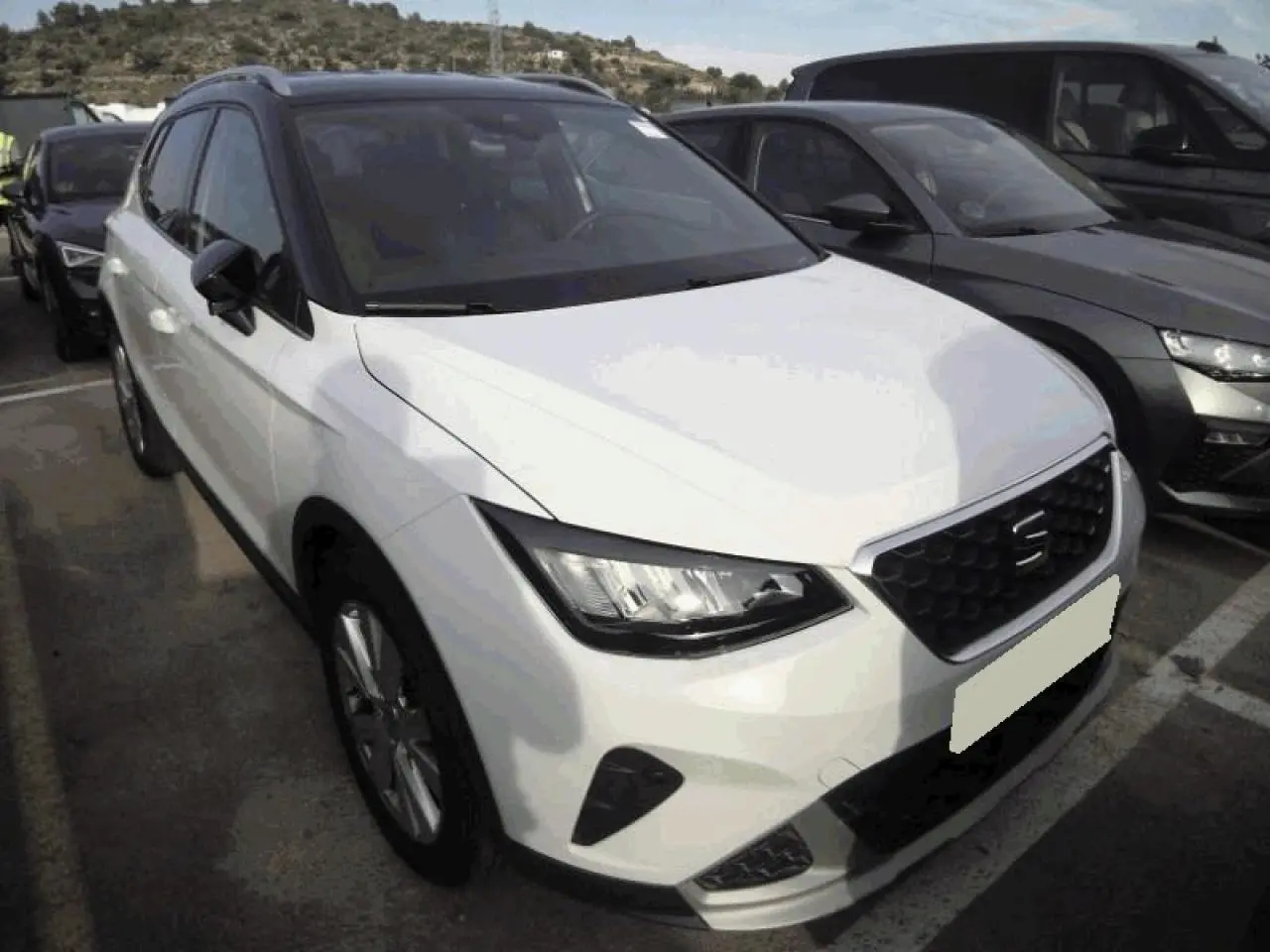 SEAT Arona blanc Nevada en vue 3/4 avant, toit noir contrasté et calandre chromée XPERIENCE visible.