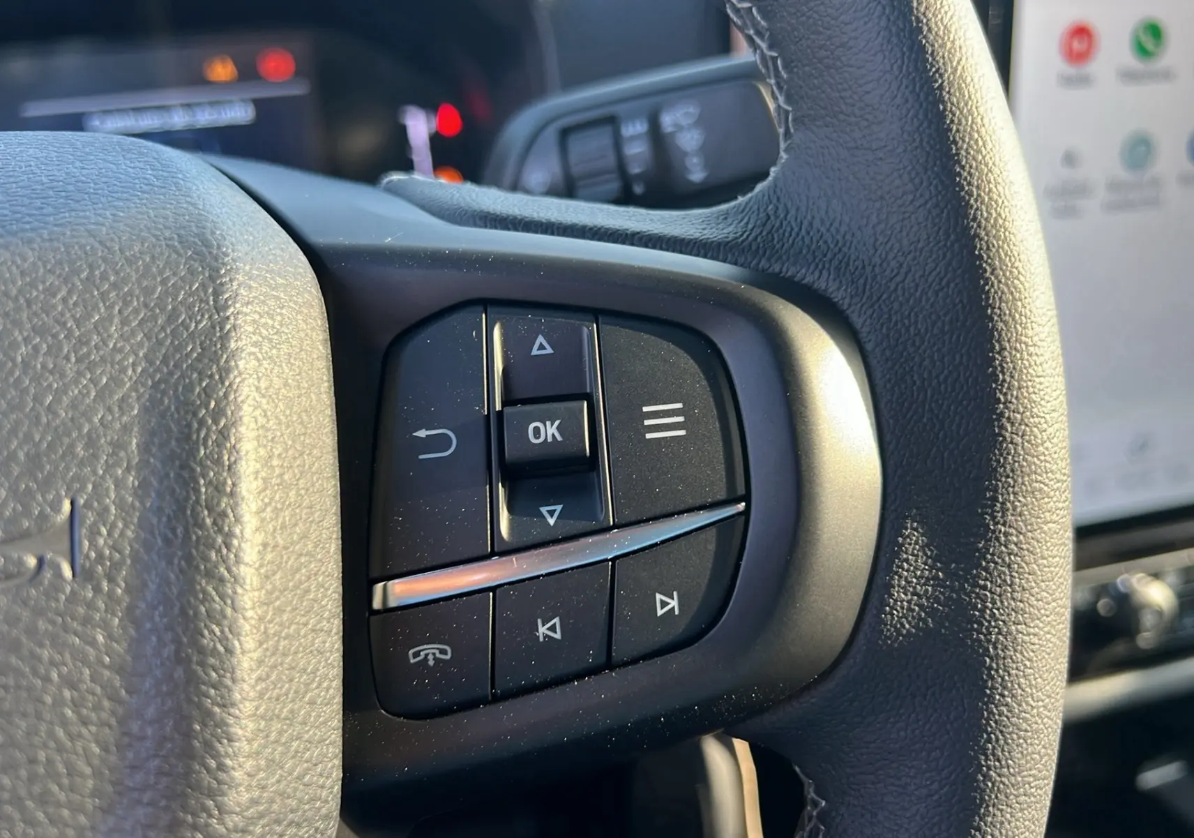 Gros plan sur les commandes multifonctions noires du volant cuir du Ford Ranger 2025, intérieur moderne avec écran tactile.