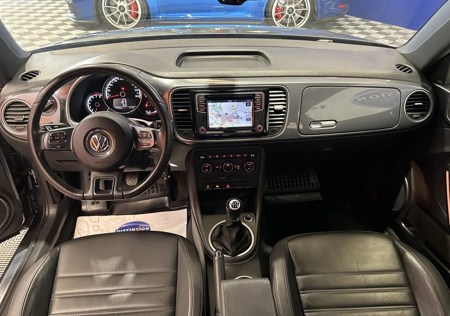 Vue intérieure frontale de la Volkswagen Coccinelle 2016 gris, avec volant cuir, GPS actif et boîte manuelle.