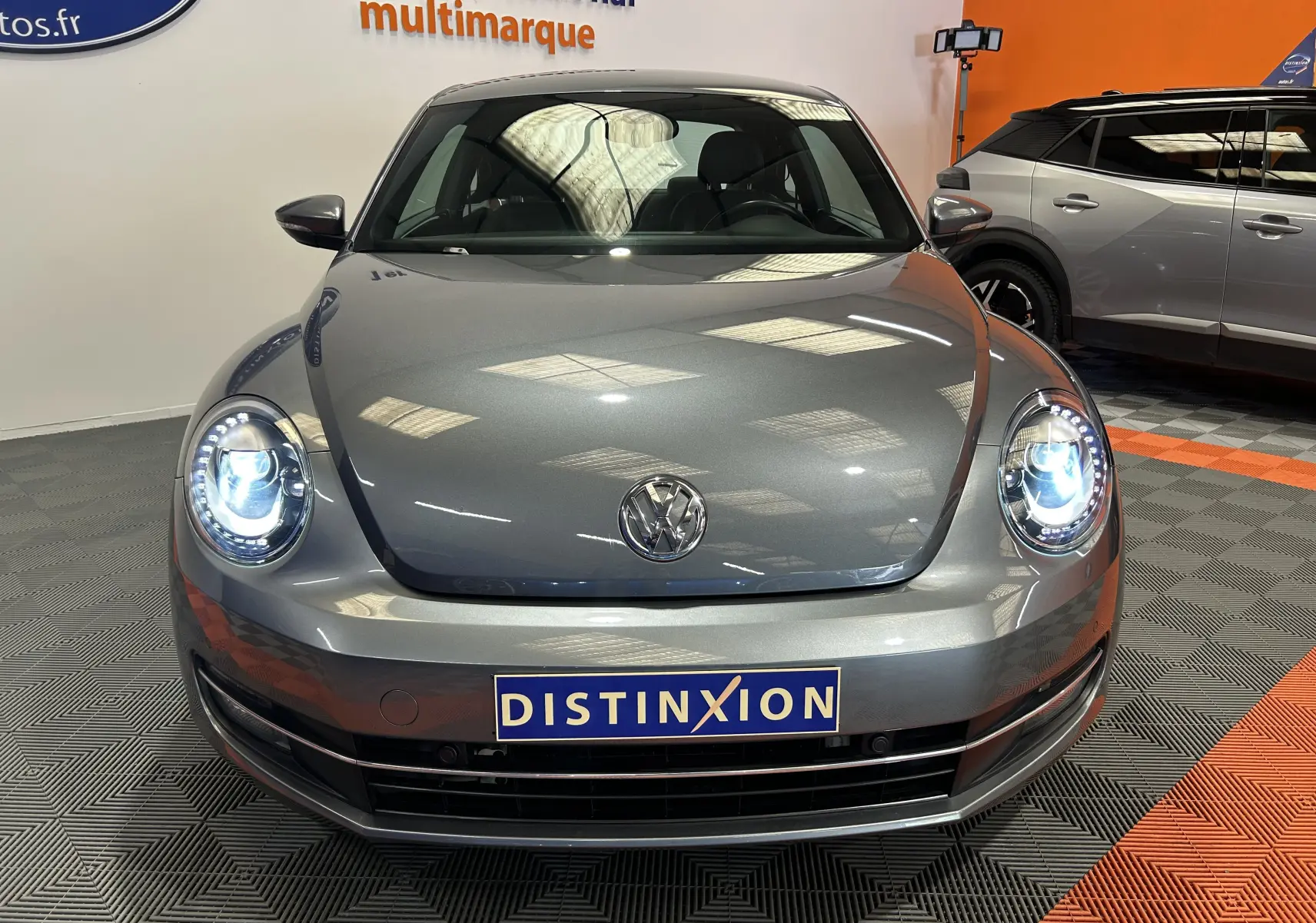 Vue avant d'une Volkswagen Coccinelle gris métallisé 2016 avec phares LED allumés dans un showroom.