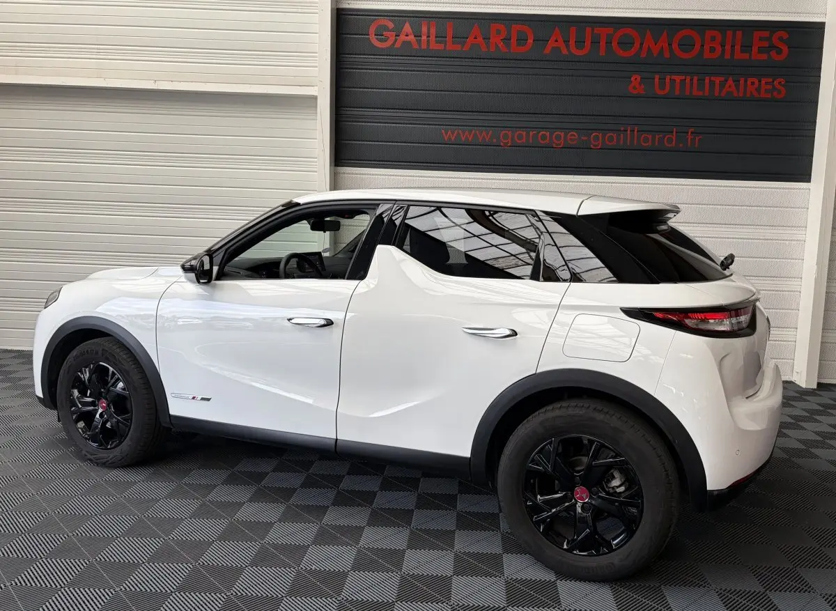 Vue de profil côté gauche d’un DS3 Crossback blanc 2022 avec jantes noires et toit noir, stationné en intérieur.