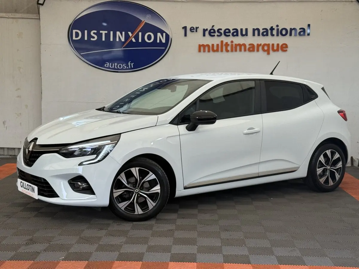 Renault Clio blanc vue de profil côté gauche, avec jantes alliage et vitres teintées en arrière-plan showroom.