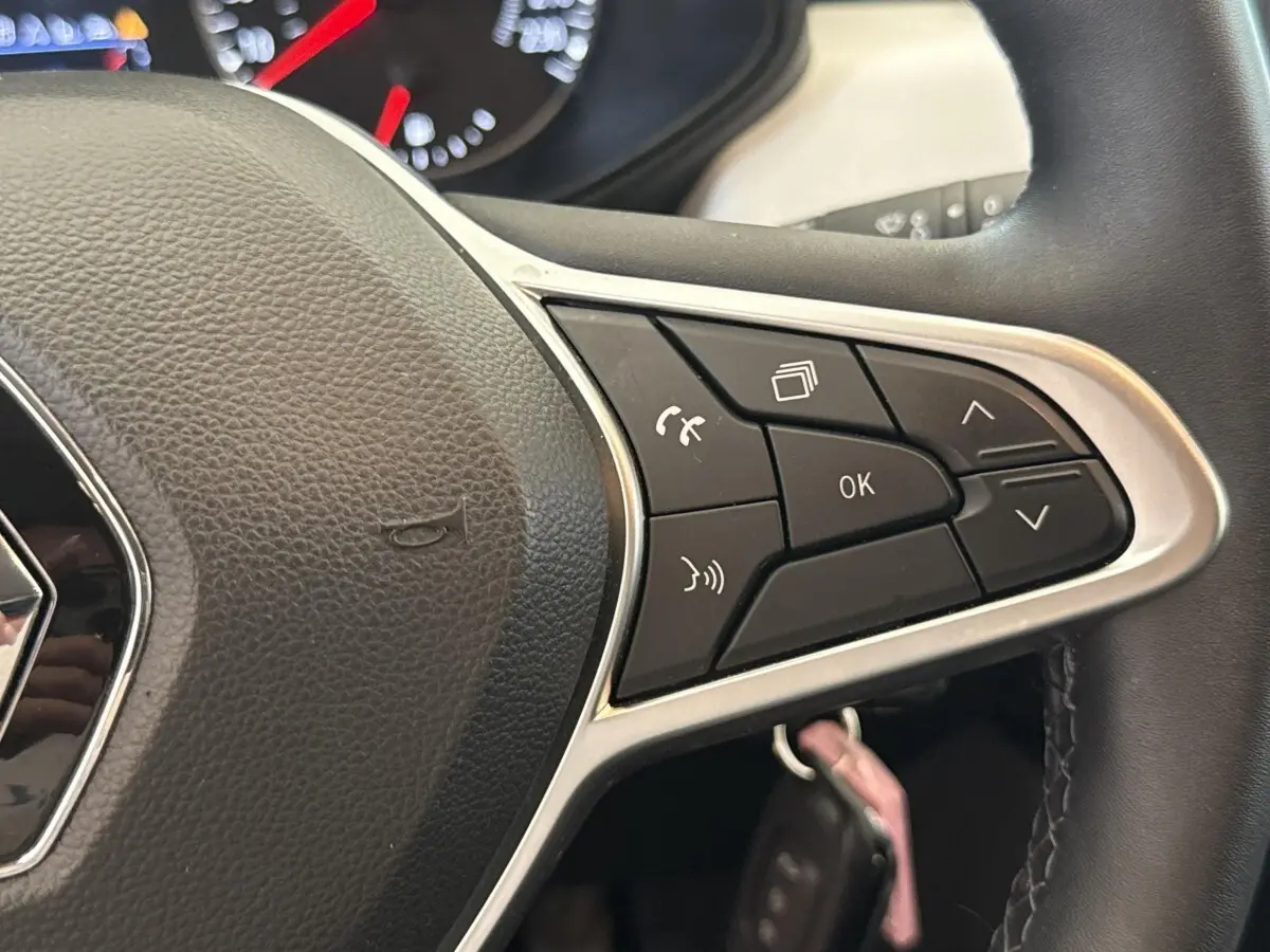Gros plan sur le volant noir de la Renault Clio blanc 2023, avec commandes multifonctions et logo Renault visible.