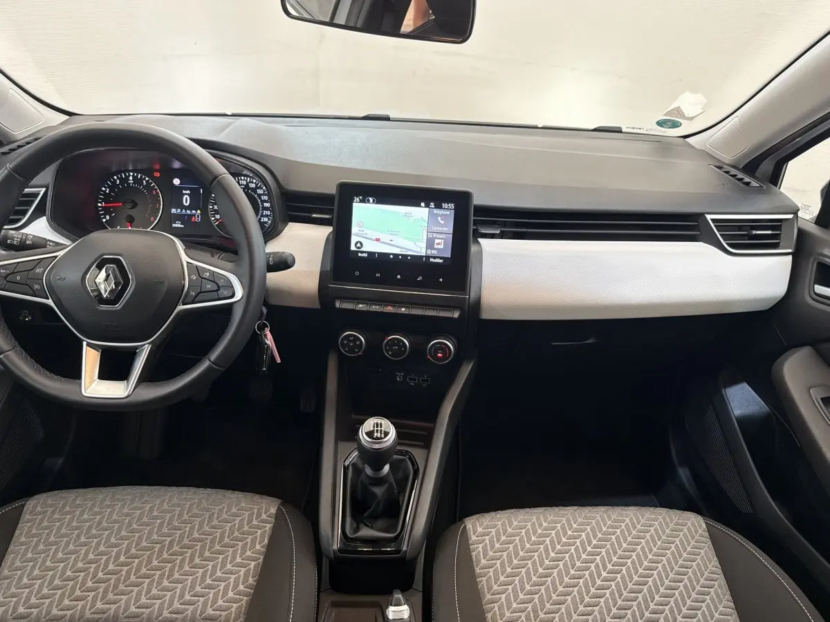Vue intérieure avant de la Renault Clio blanche 2023, tableau de bord avec écran tactile et volant cuir multifonctions.