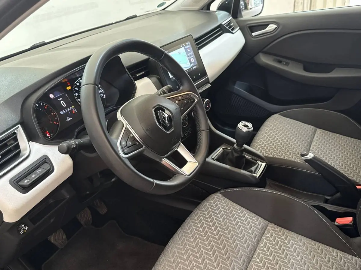 Vue intérieure côté conducteur de la Renault Clio blanche 2023, volant cuir, écran tactile central et levier de vitesse manuel.