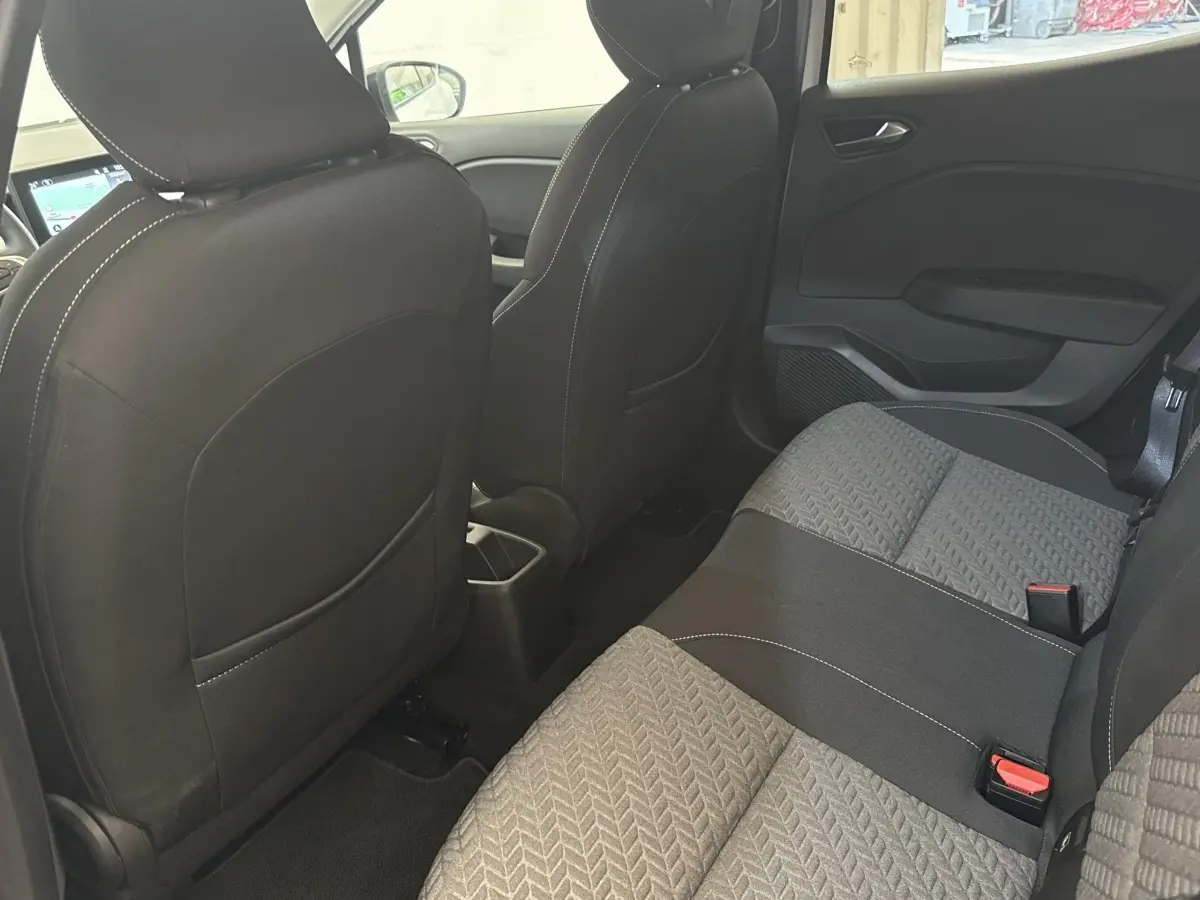 Vue intérieure arrière de la Renault Clio blanche 2023, montrant la banquette tissu bicolore et les dossiers des sièges avant.